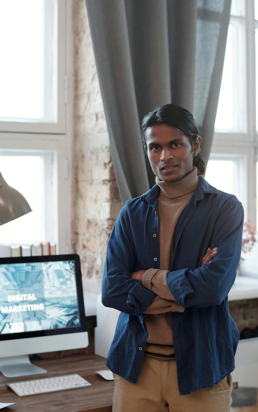 Young man posing confidently in his own company with digital marketing displayed on the computer screen.